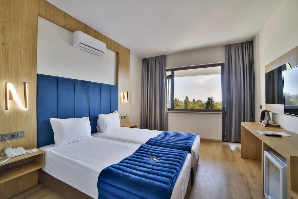 A hotel room with two beds, a TV, a desk, and a window with curtains.