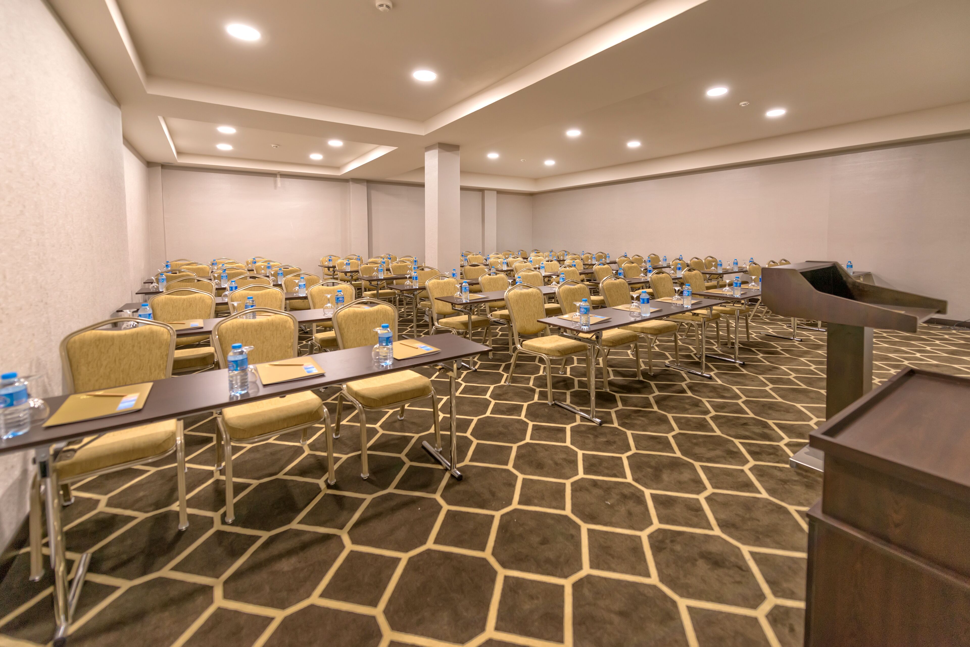 Un salón de conferencias con varias mesas y sillas, equipado con botellas de agua y tarjetas de identificación.