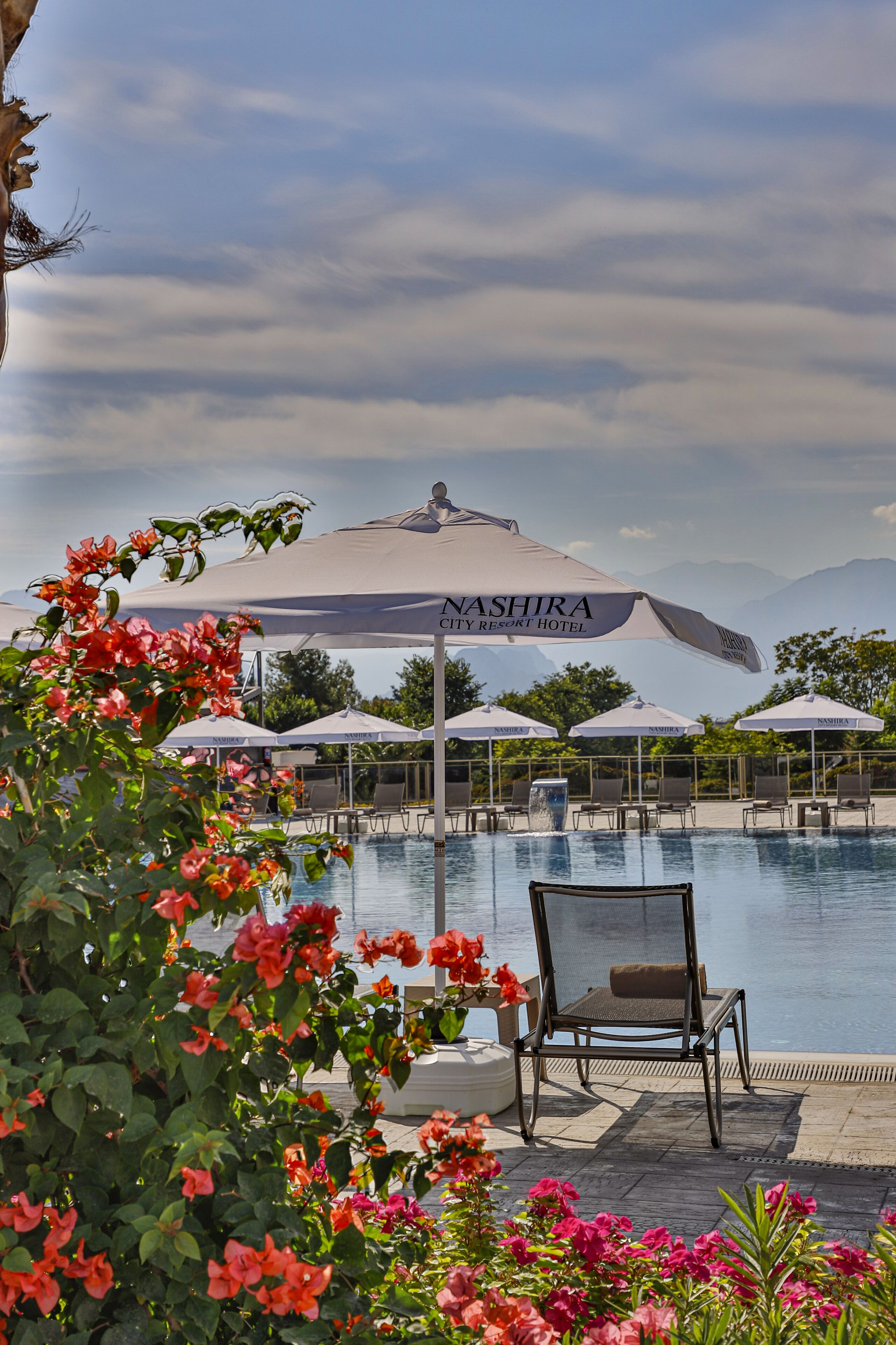 Et poolområde med liggestole og parasoller ved NASHIRA City Resort Hotel.