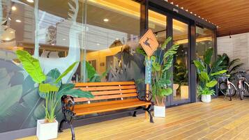 Un banc devant un bâtiment doté de grandes fenêtres, de plantes en pot et d’un vélo.