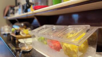 A counter with a clear plastic container holding a yellow beverage, a green cup, and a red cup.