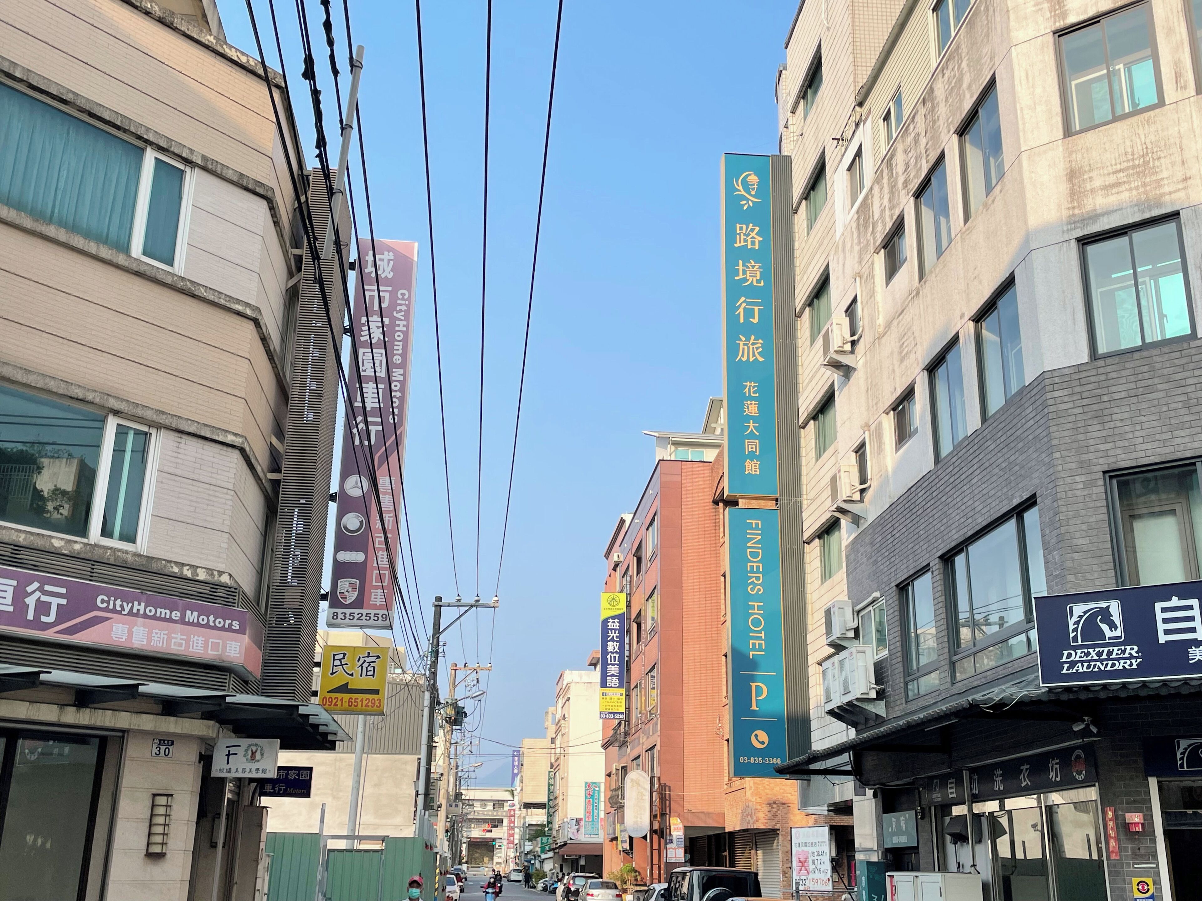 A street with various commercial buildings, including a hotel and a laundry service.