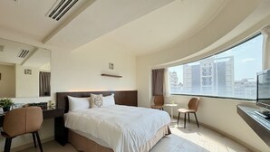 A hotel room with a large bed, a desk with a chair, a small table, and a large window offering a city view. - Finders Hotel Hualien Da-Tong (Hualien City)
