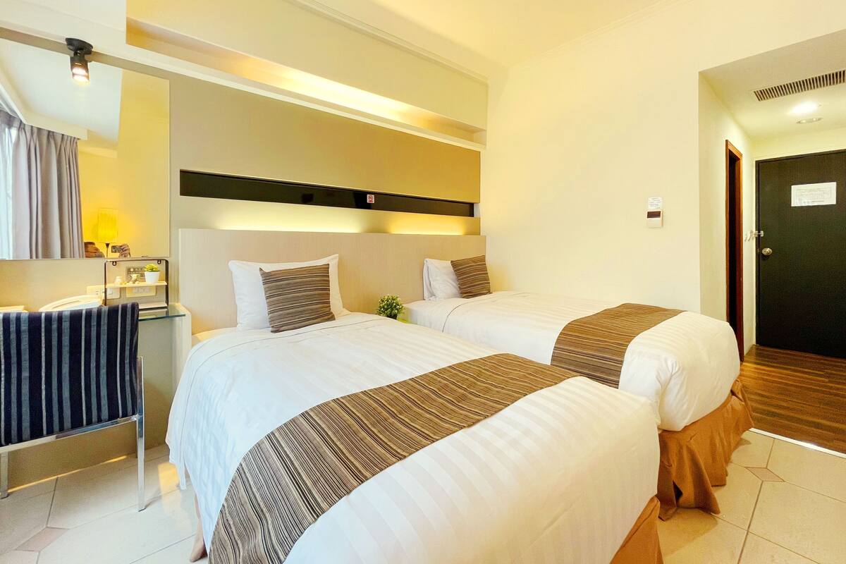 Habitación de hotel con dos camas, una mesita de noche, un espejo y una puerta.