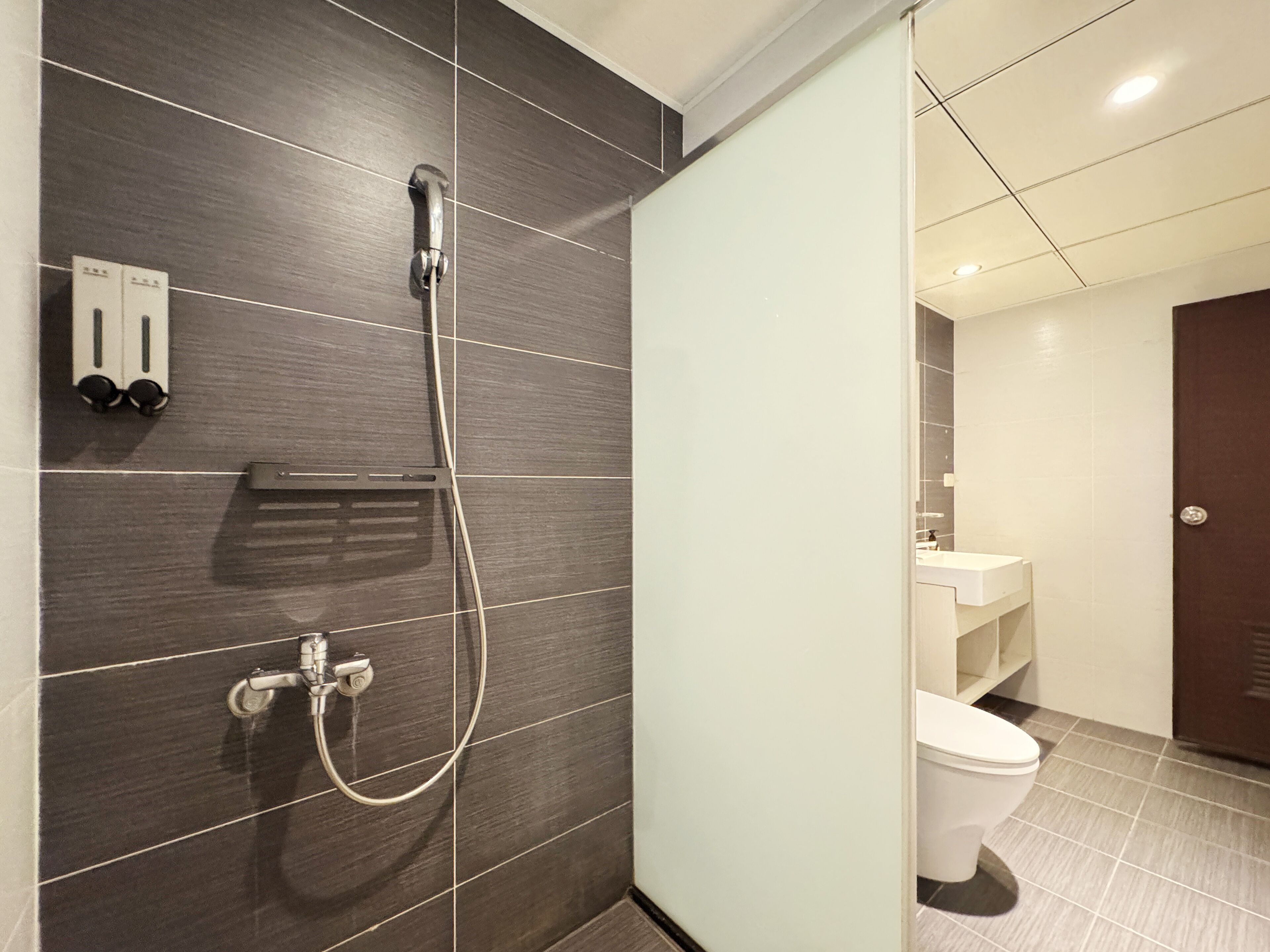 A modern bathroom with dark tiled walls, a shower with a handheld hose, and a toilet.