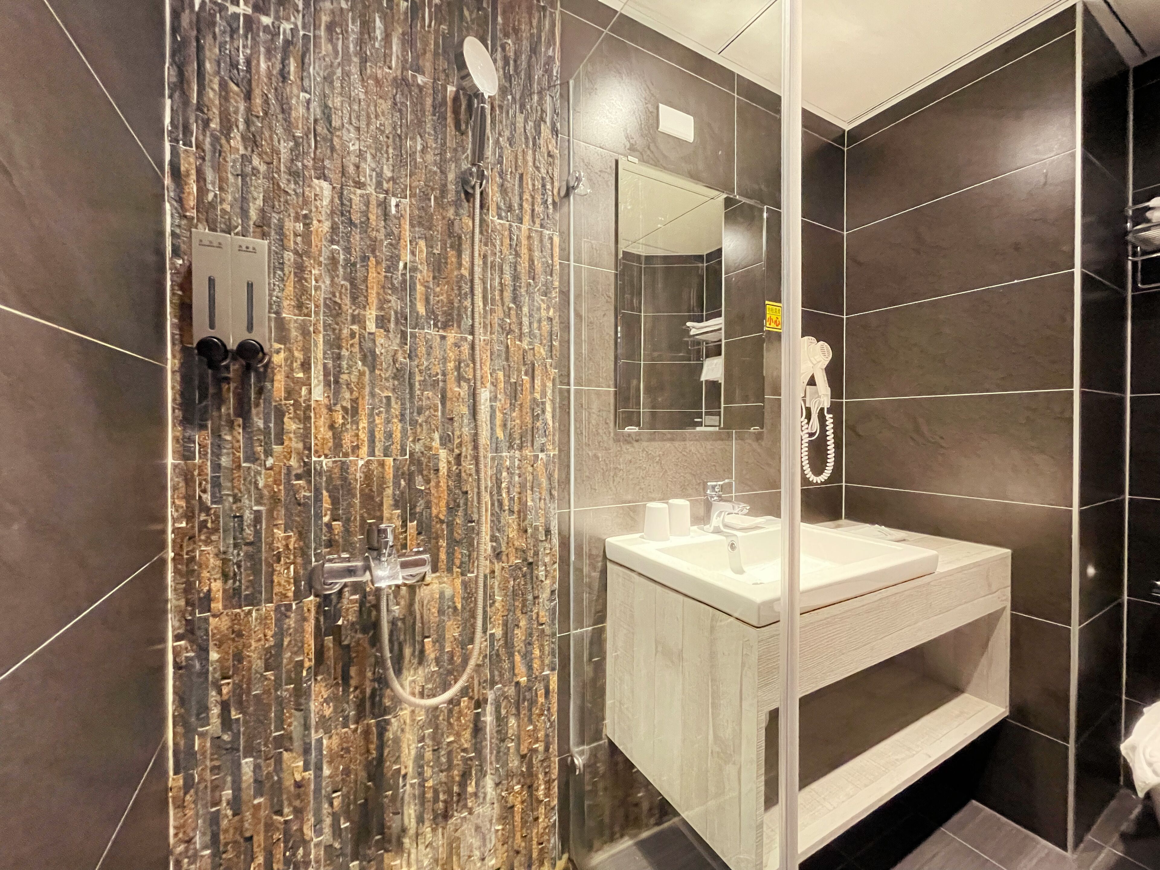 A modern bathroom with a stone-textured shower wall, a white sink, and a mirror above the sink.