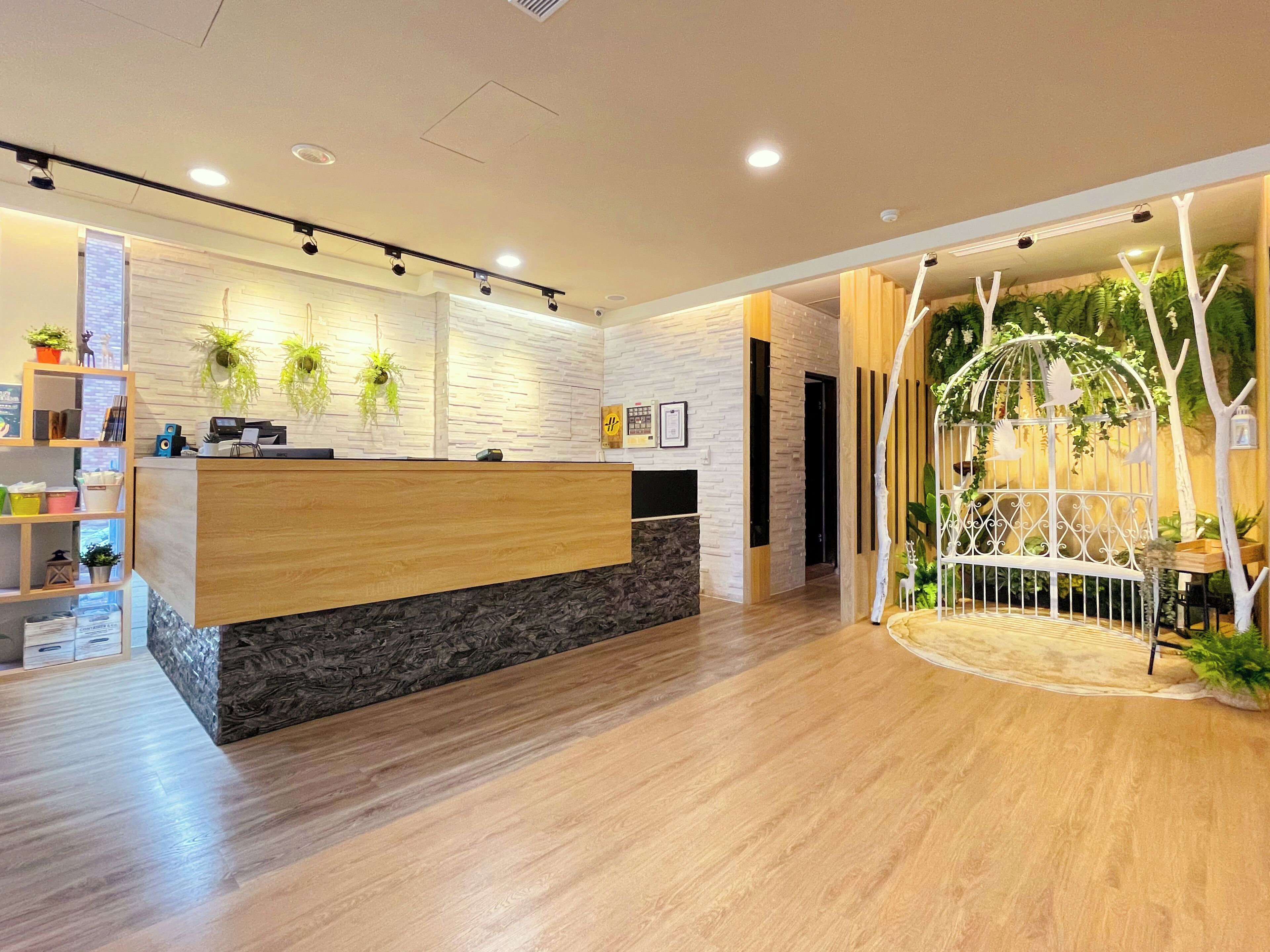 A reception area with a wooden reception desk, a stone accent wall, and a wooden floor. There are potted plants on the wall and a decorative birdcage with greenery.