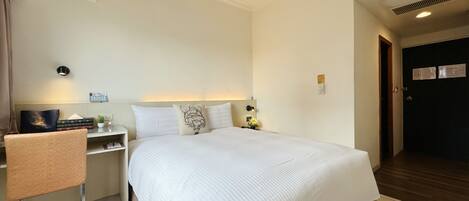 A hotel room with a large bed, a desk with a chair, a nightstand, and a wall-mounted light.