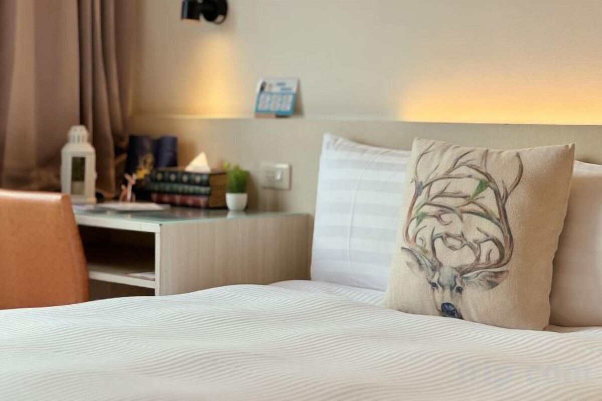 A hotel room with a bed, a nightstand, a lamp, and a wall-mounted camera.