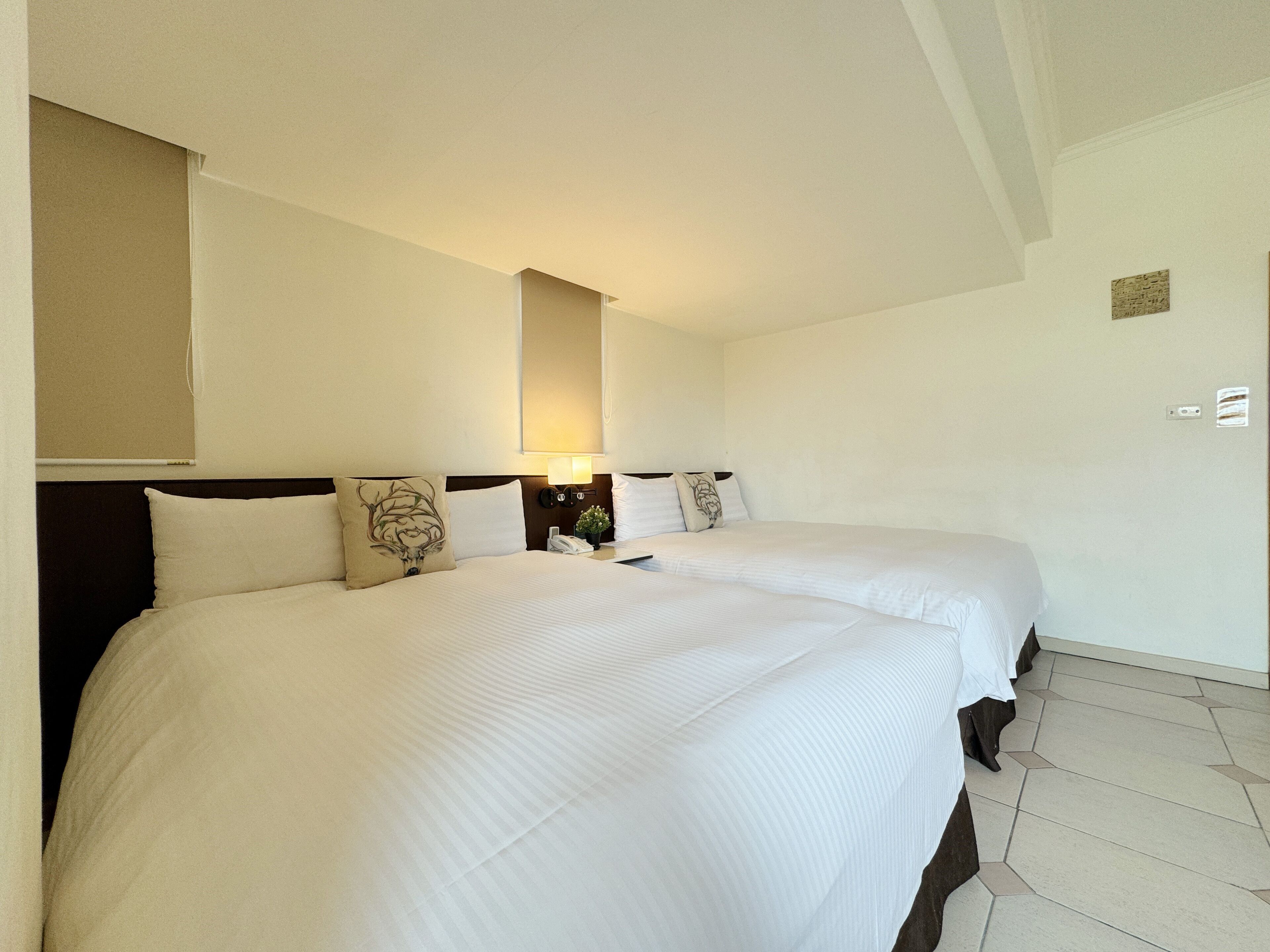 A hotel room with two beds, a nightstand with a lamp, and a wall-mounted mirror.