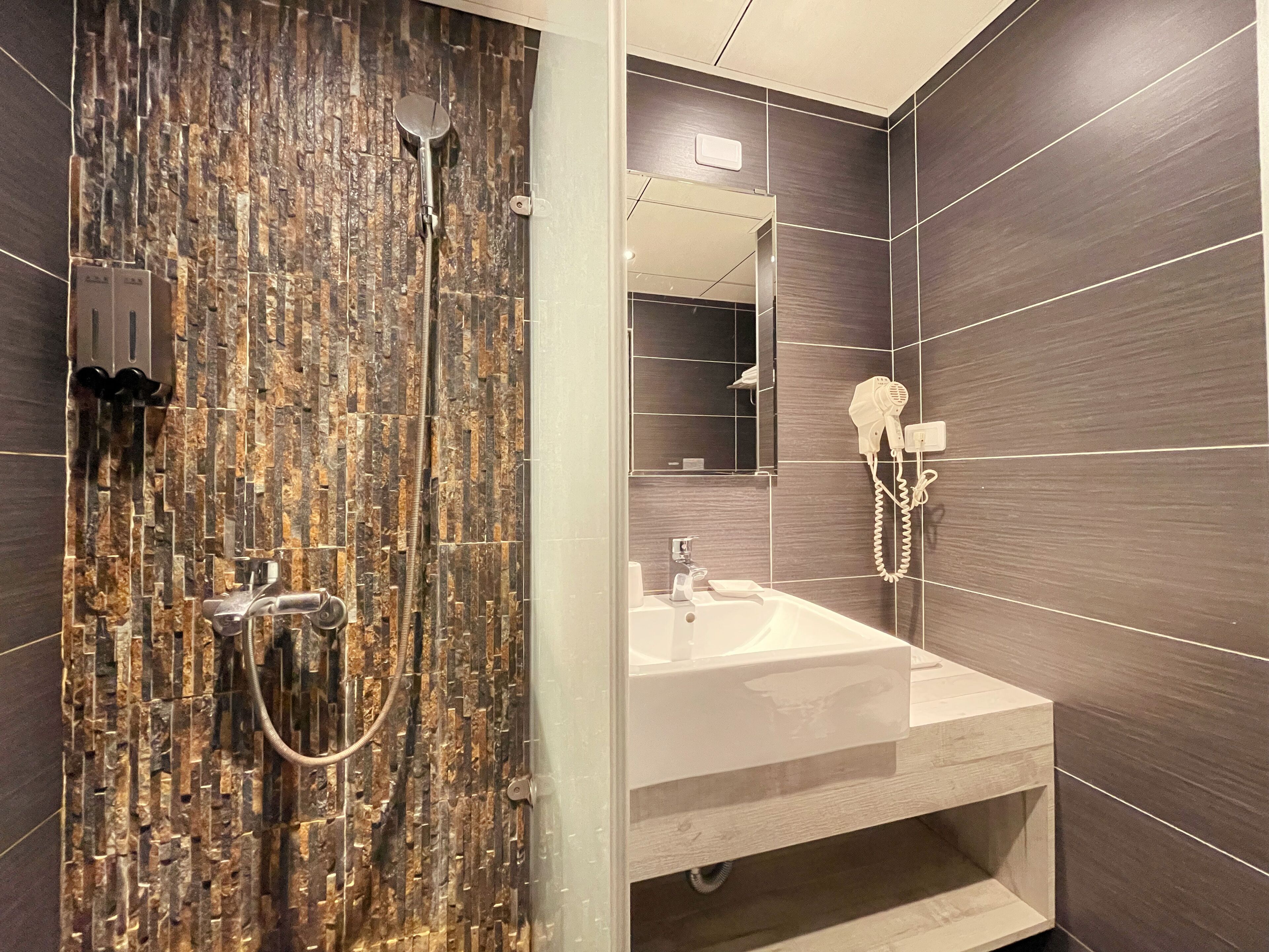 A modern bathroom with a shower, a sink, and a hairdryer mounted on the wall.