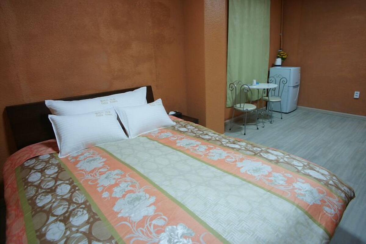 A hotel room with a bed, a small table with chairs, and a refrigerator.
