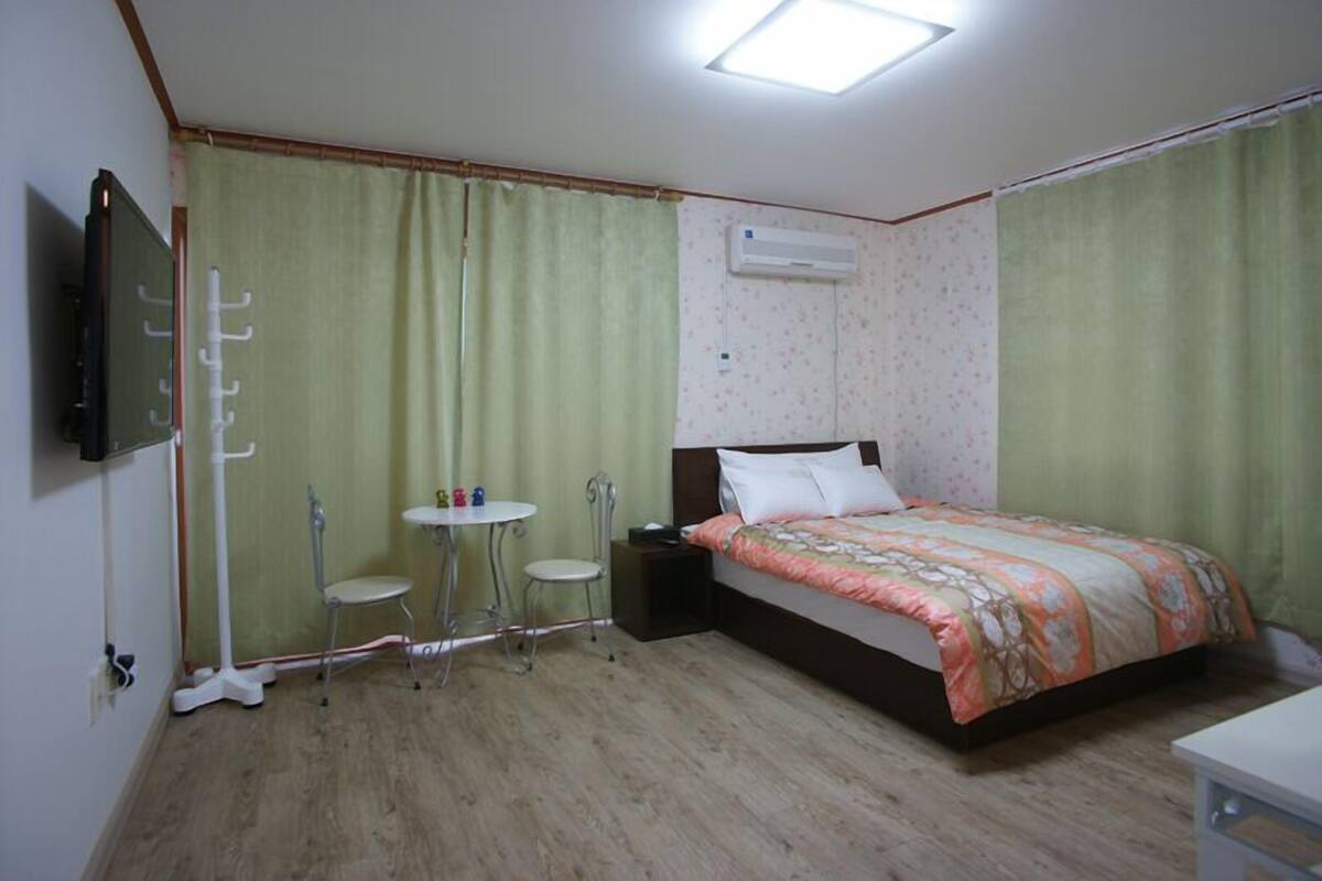 A bedroom with a bed, a bedside table, a small table with chairs, and a TV mounted on the wall.