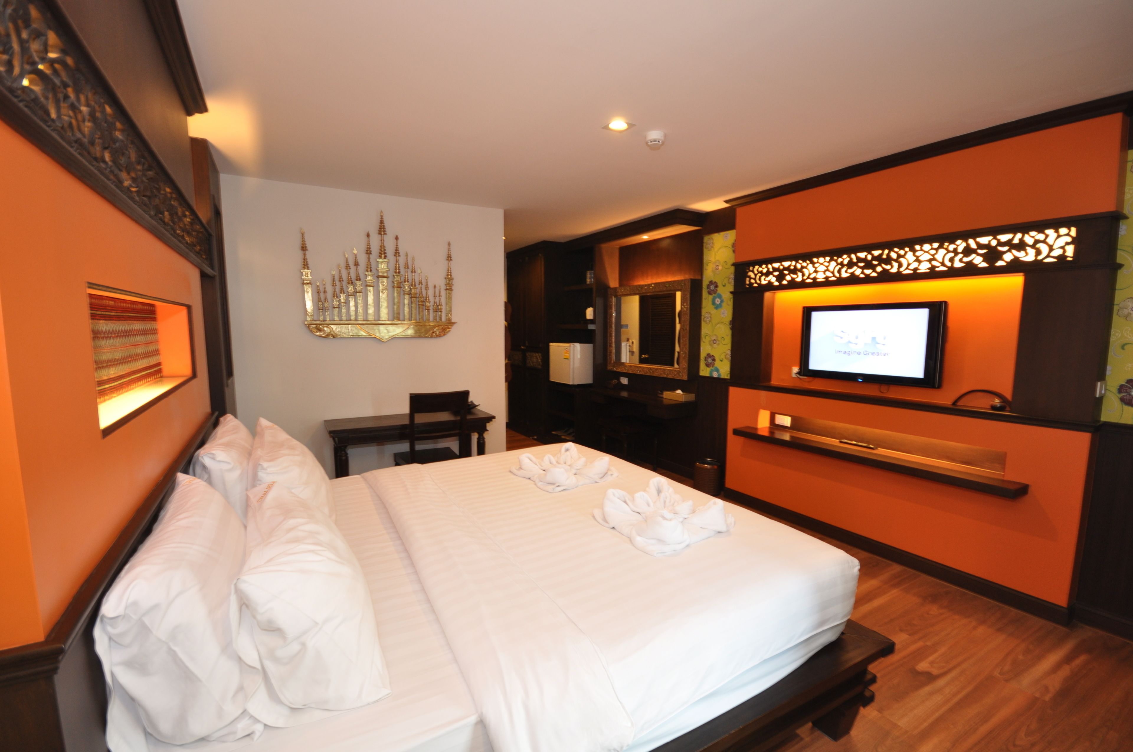 A hotel room with a large bed, a television, a chandelier, and a desk.