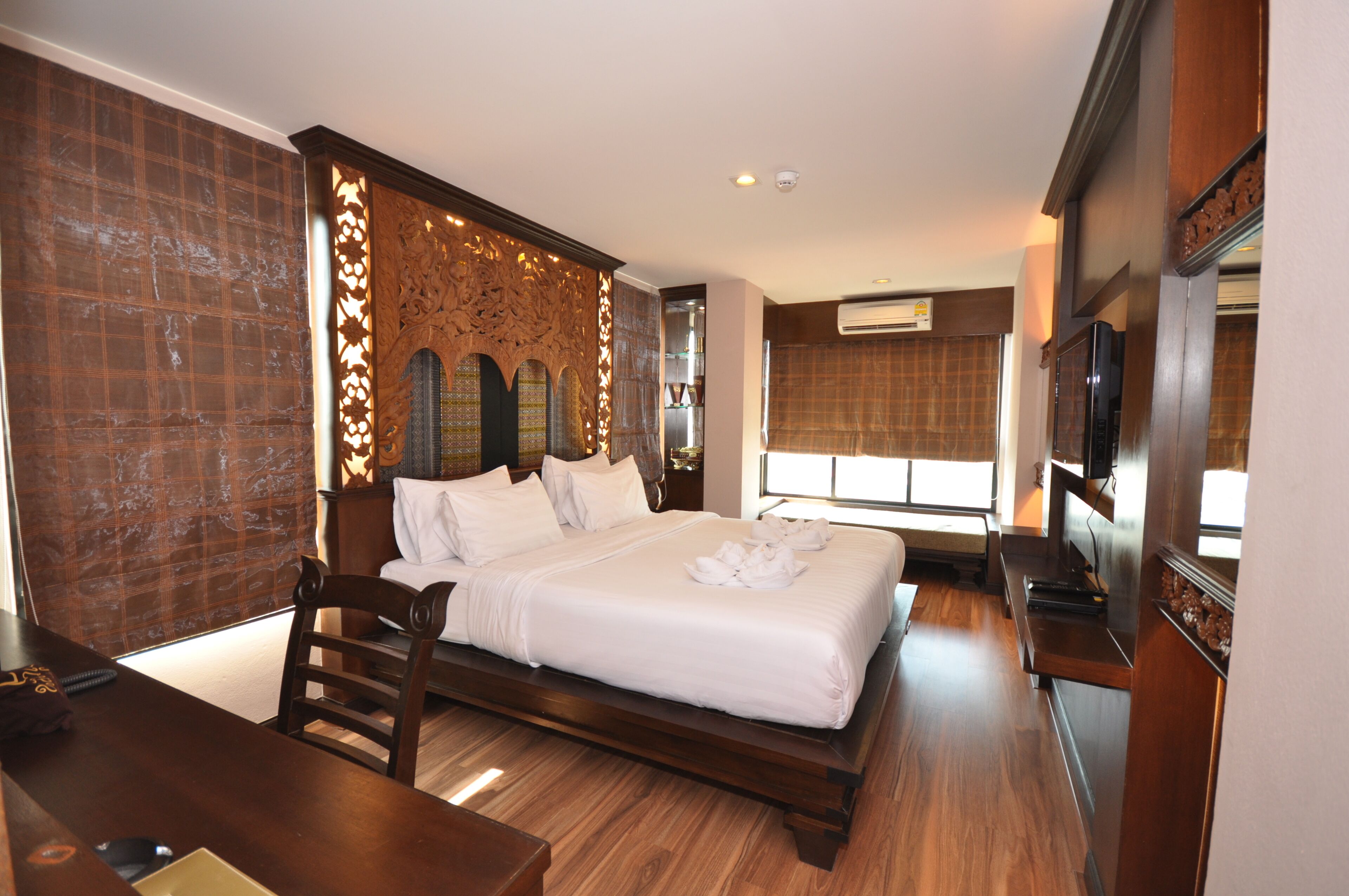 A hotel room with a large bed, wooden headboard, a desk, and a television.