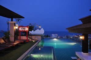 A rooftop pool with a view of the sea, lounge chairs, and a sign with Thai text. - Chalelarn Hotel (Hua Hin)