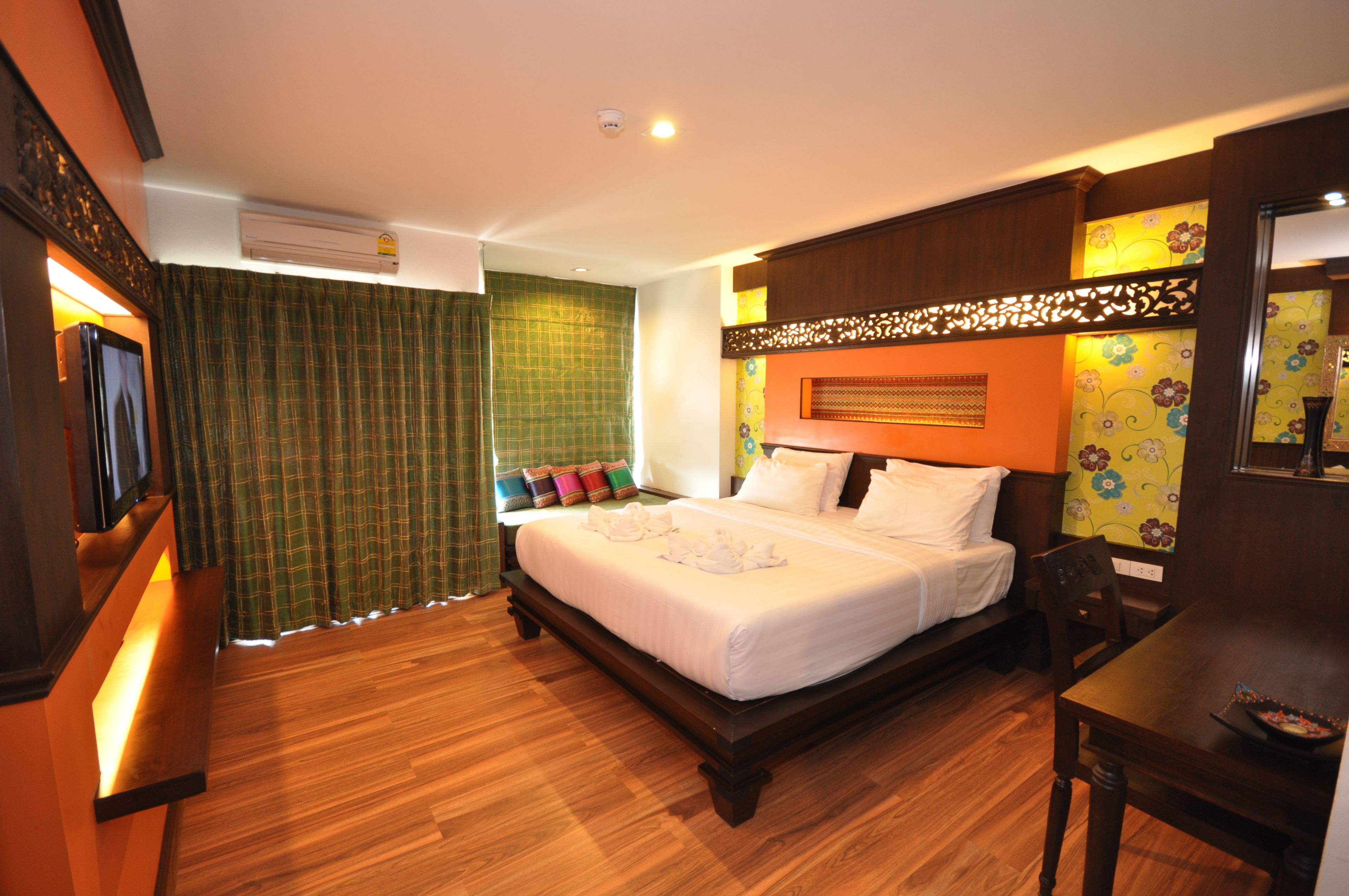 A hotel room with a large bed, a wooden floor, a desk, and a television.