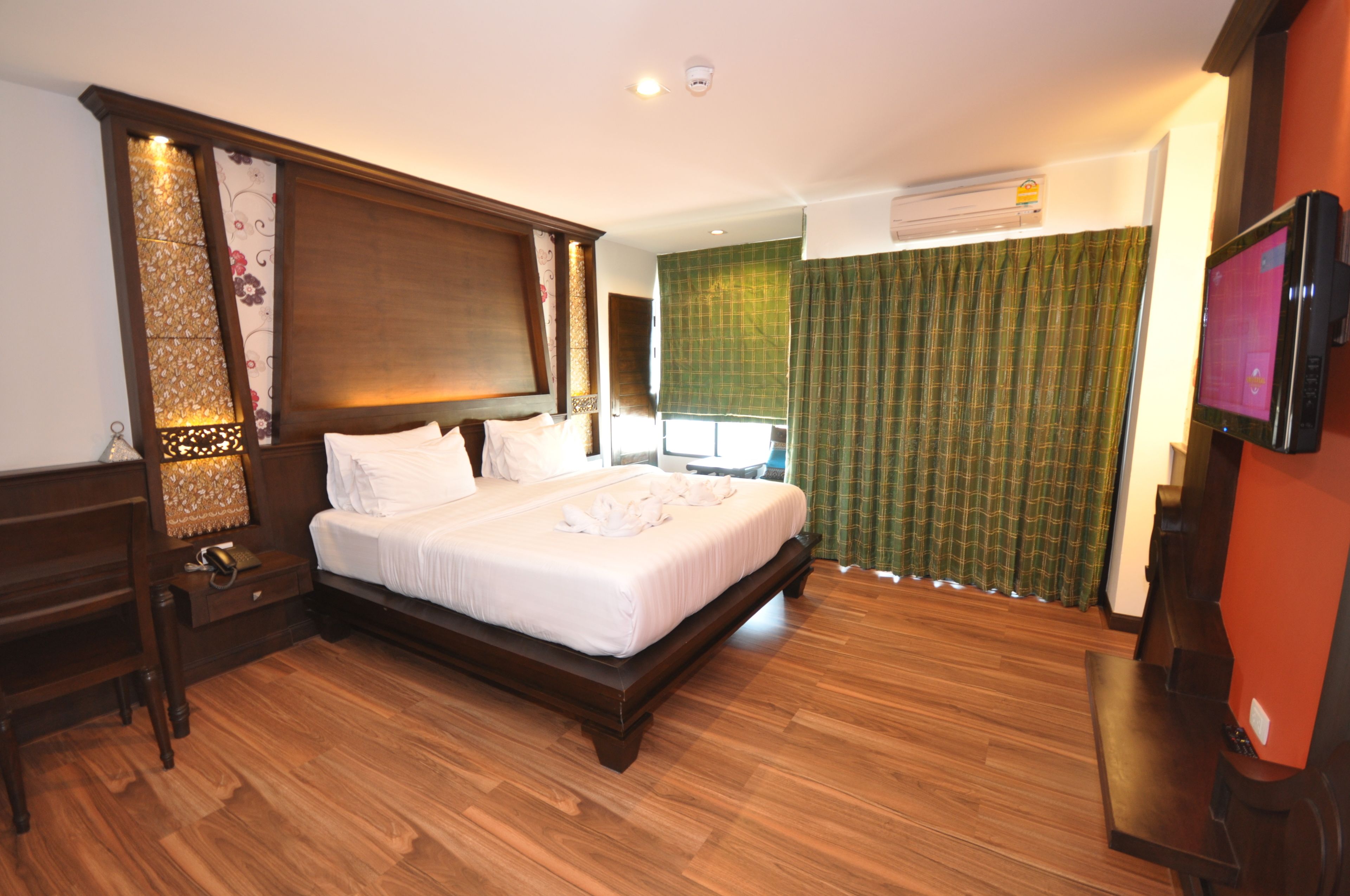 Habitación de hotel con una cama grande, suelo de madera, televisor y una ventana con cortinas.
