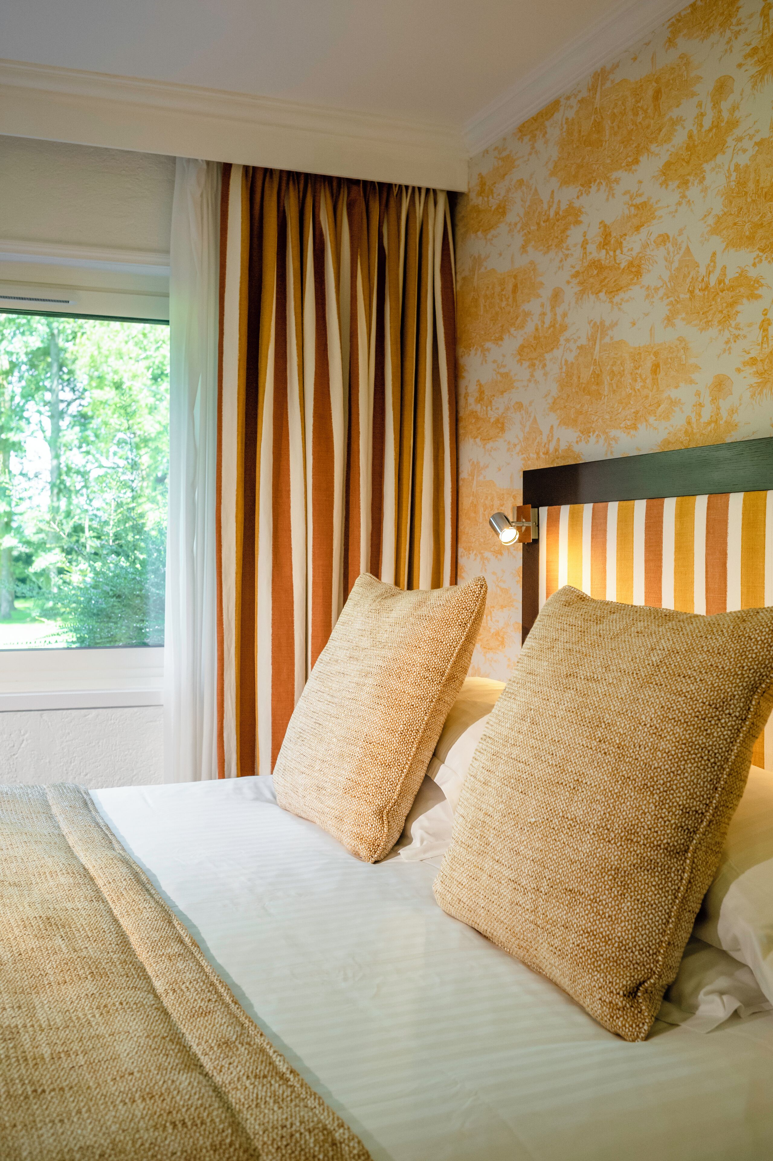 A hotel room with a bed, striped curtains, and a wall with floral wallpaper.