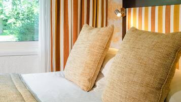 A hotel room with a bed, striped curtains, and a wall with floral wallpaper.