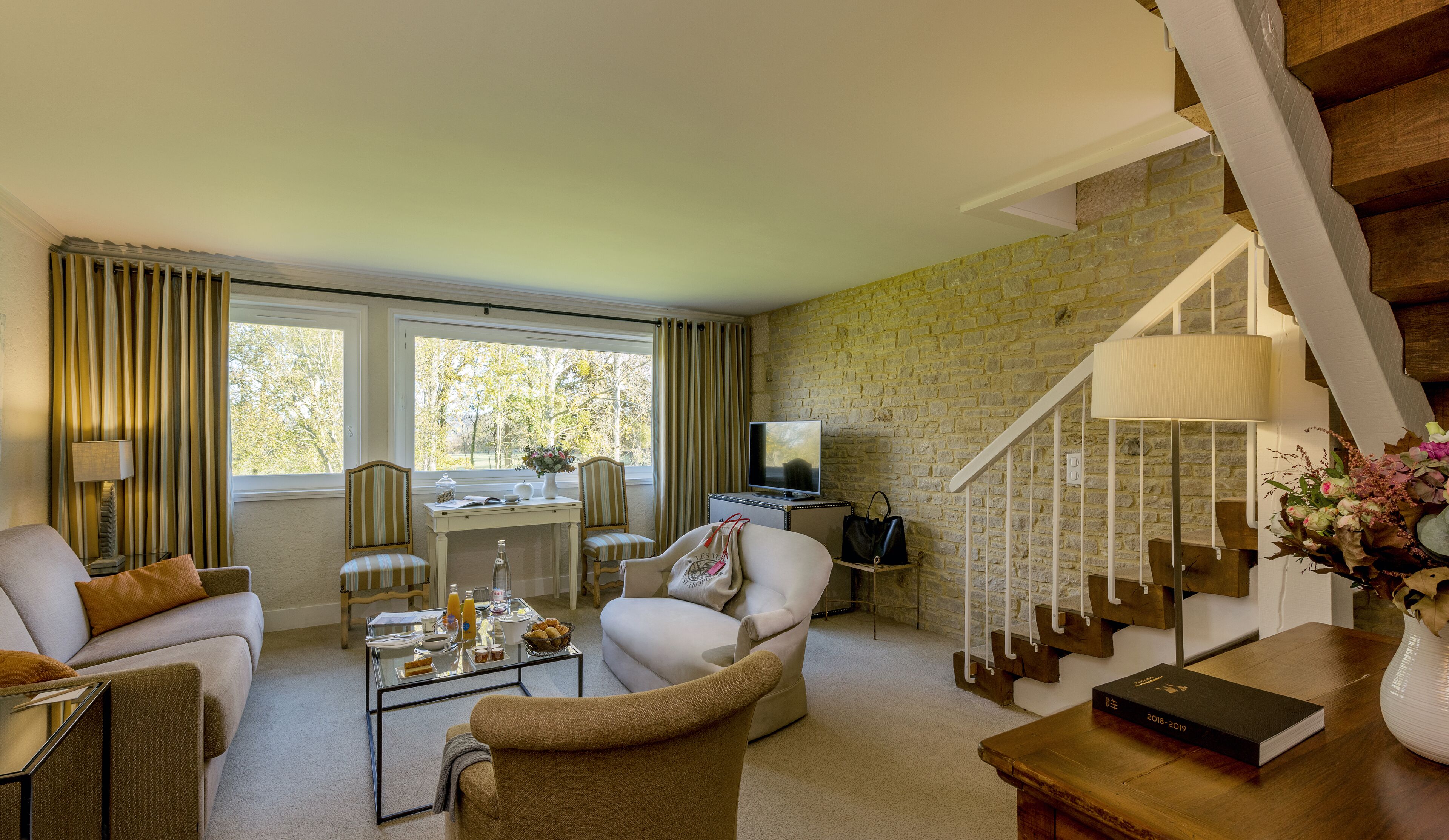 A living room with a sofa, armchairs, a coffee table, a TV, and a staircase.