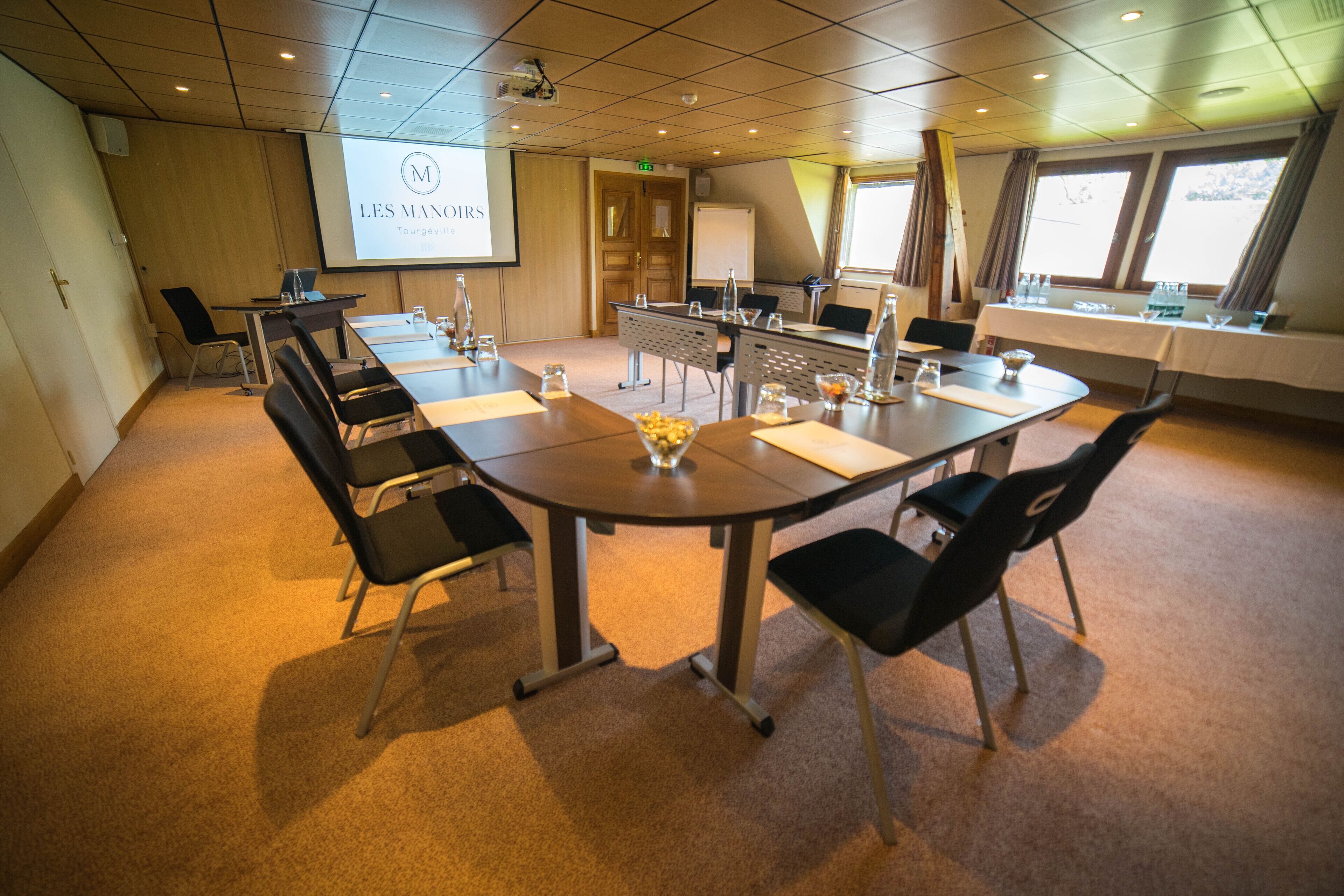 Une salle de conférence équipée d’une longue table, de chaises, d’un écran de projection et d’un tableau blanc.