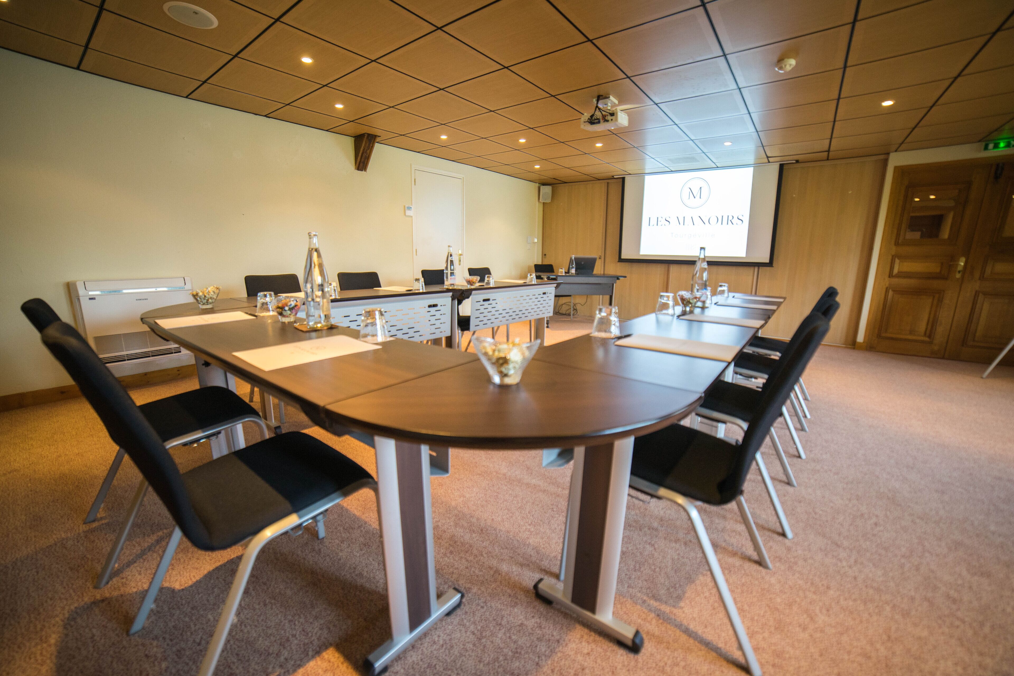 Een vergaderruimte met een grote tafel, stoelen, een projectiescherm en een whiteboard.