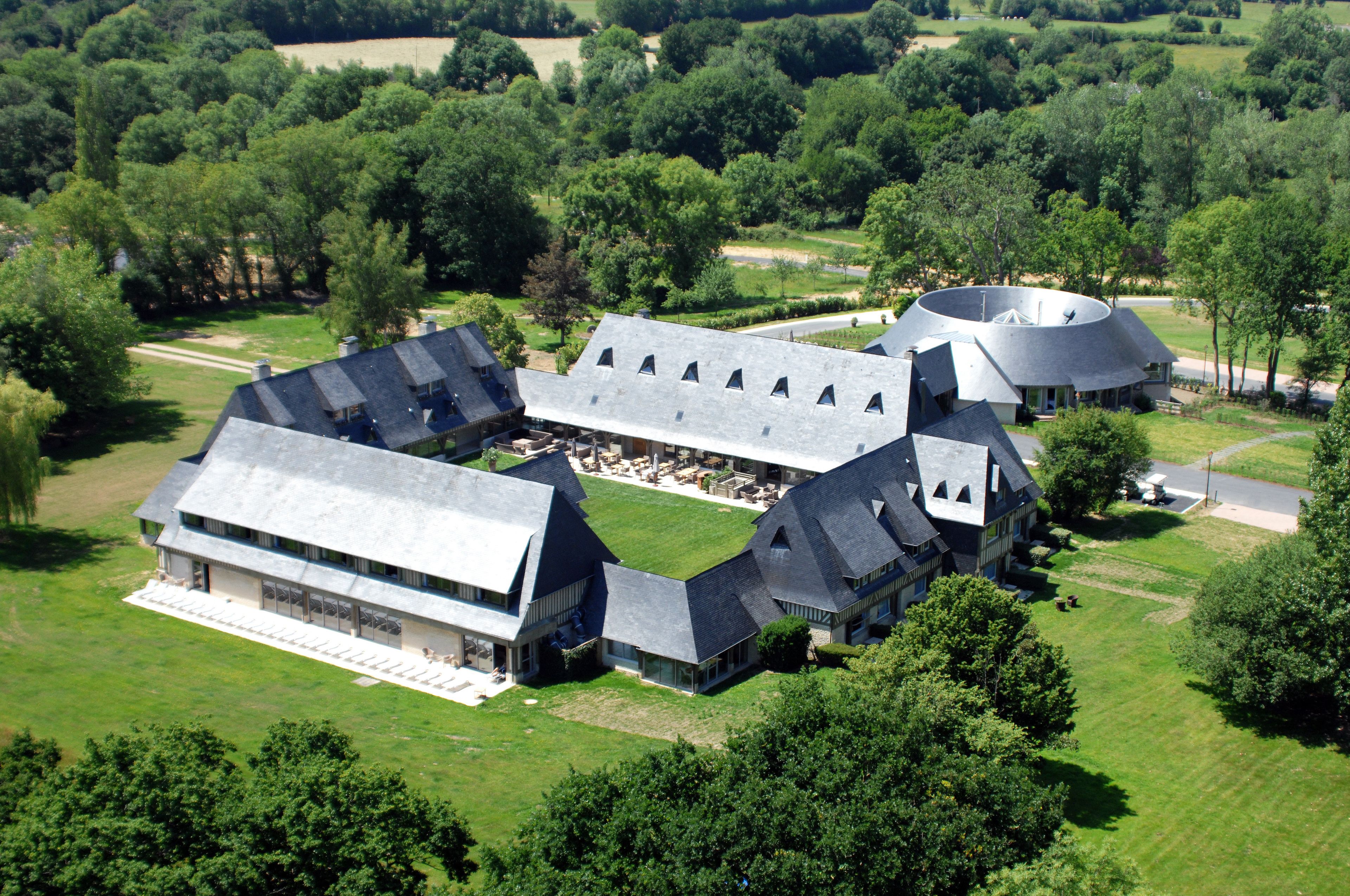 A large, modern building with multiple sections, surrounded by lush greenery and trees.