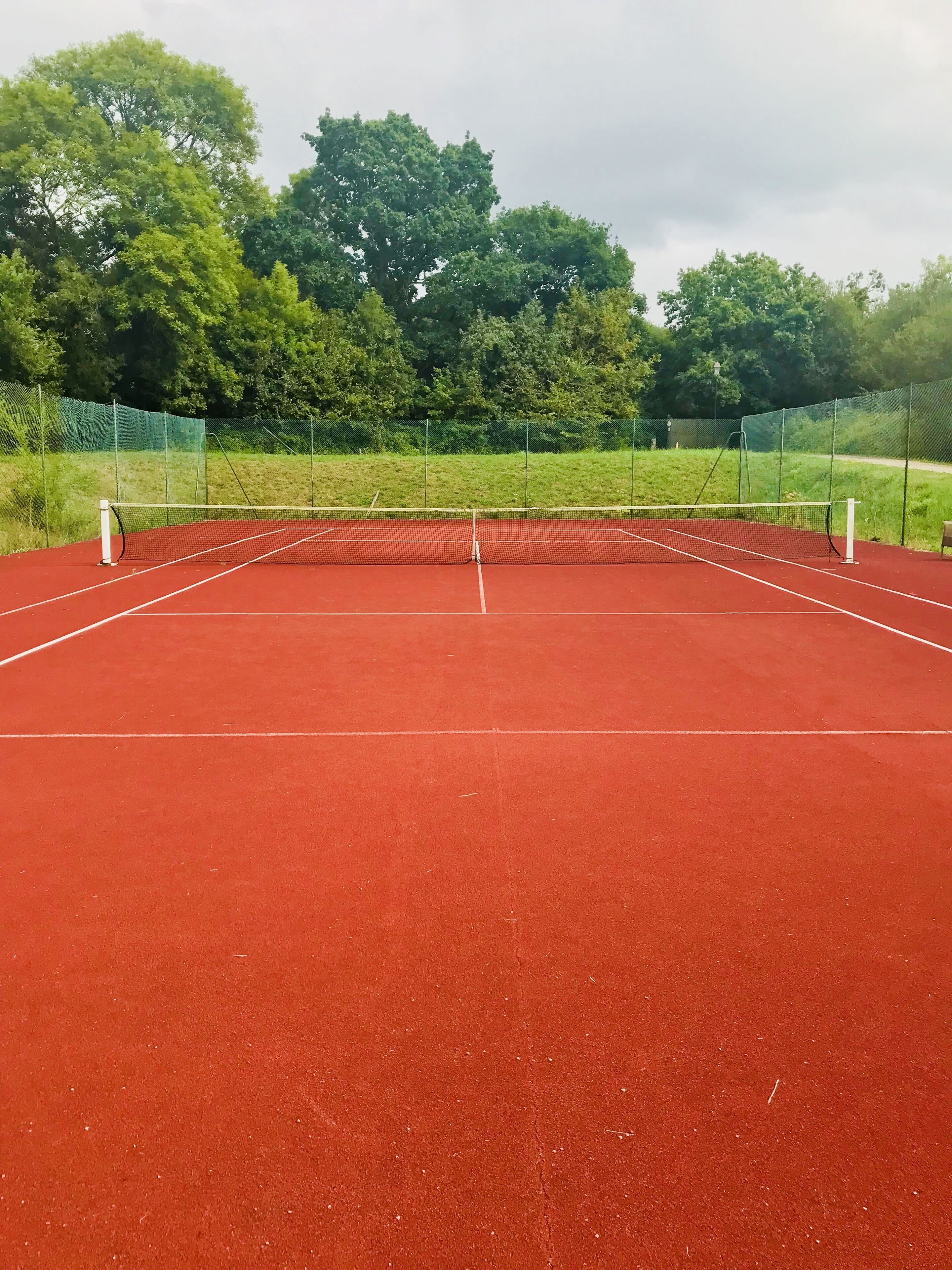 A tennis court with a red surface and white boundary lines.
