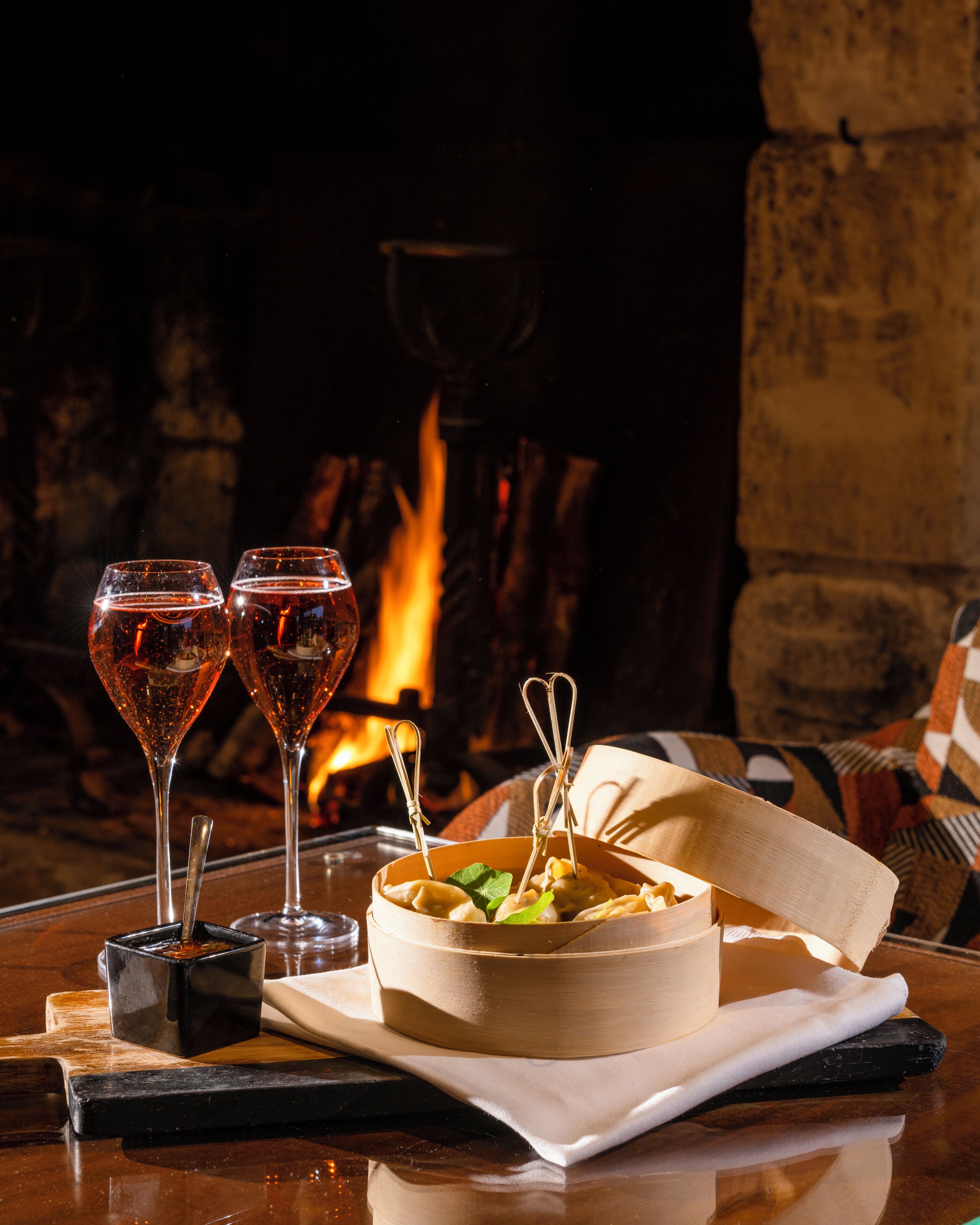 Une table à manger avec un saladier en bois rempli de nourriture, deux verres de vin et un petit plat contenant des condiments.