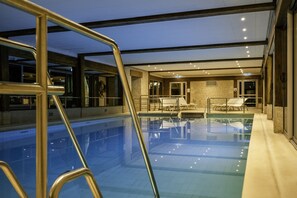 An indoor swimming pool with clear water, a metal ladder, and a lounge area with chairs and a table. - Les Manoirs de Tourgéville (Tourgeville)