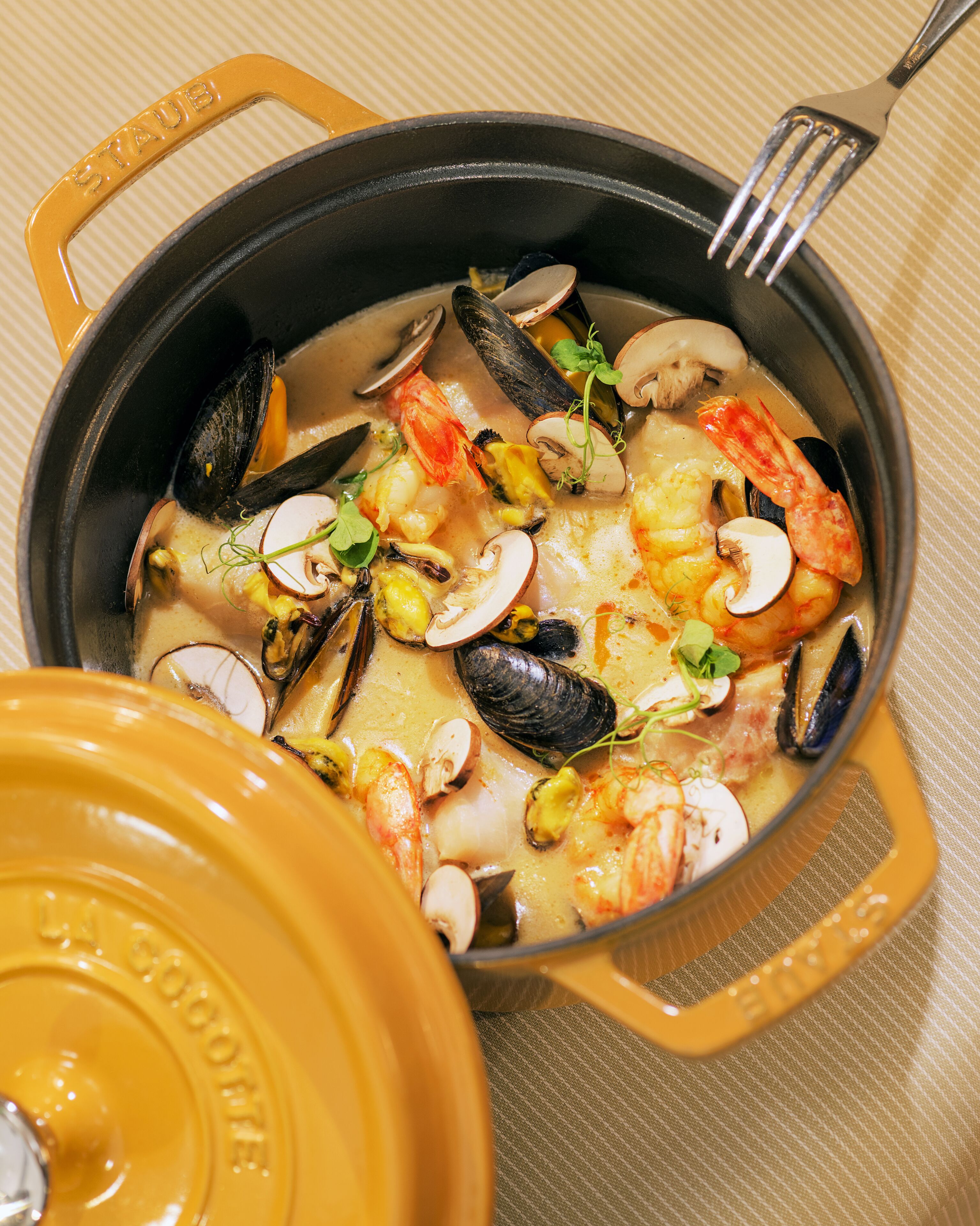 A pot of seafood stew with mussels, shrimp, and mushrooms.