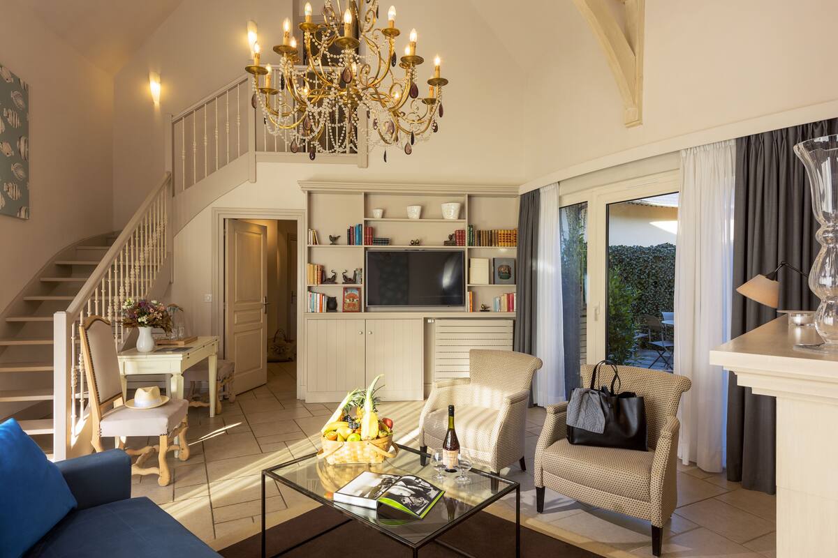 A spacious living room with a staircase, a chandelier, a television, and a bookshelf.