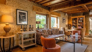 A cozy living room with a stone wall, wooden beams, a patterned sofa, and a bookshelf. - Les Manoirs de Tourgéville (Tourgeville)