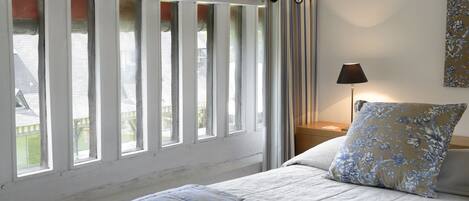 Un dormitorio con cama, mesita de noche, lámpara y ventana con cortinas.