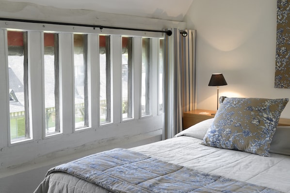 Ein Schlafzimmer mit Bett, Nachttisch, Lampe und einem Fenster mit Vorhängen.