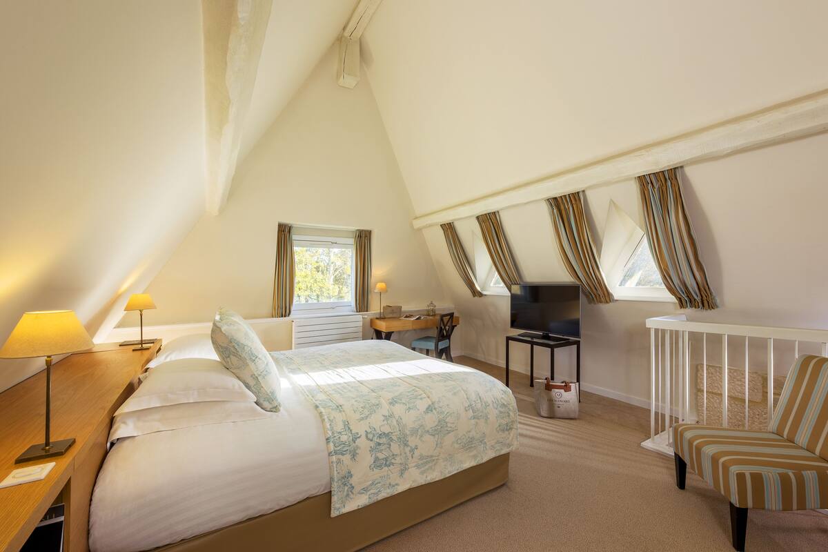 A bedroom with a bed, bedside table, lamp, desk, chair, and a crib.
