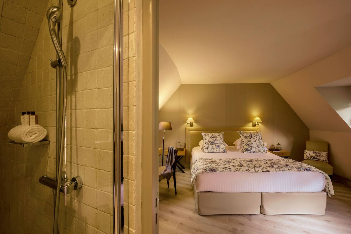 A bedroom with a large bed, a shower, and a small table with a lamp.