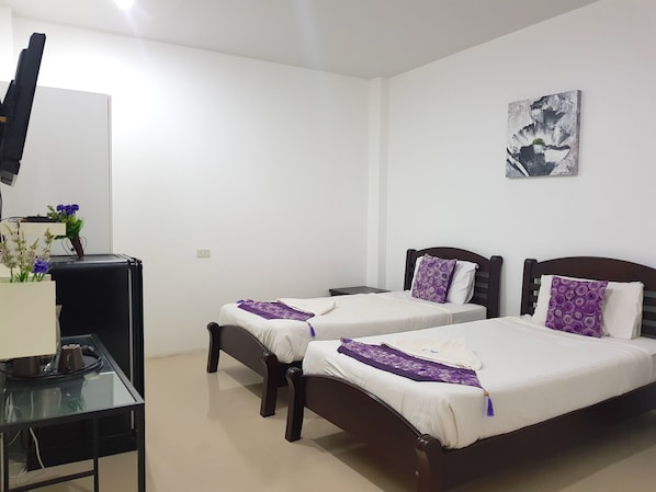 A hotel room with two single beds, a TV, a desk with a computer, and a small plant.
