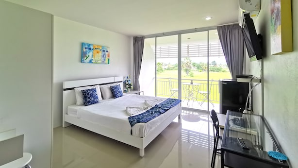 A modern hotel room with a large bed, a desk with a computer, a TV, and a balcony with a view of the garden. - Phet Cha-am Plaza & Resort (Cha-am)