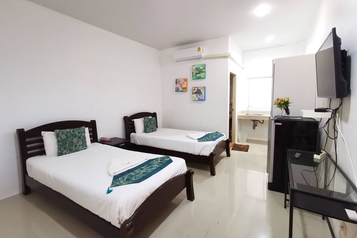 Habitación de hotel con dos camas, televisión, escritorio y baño visible a través de una puerta abierta.