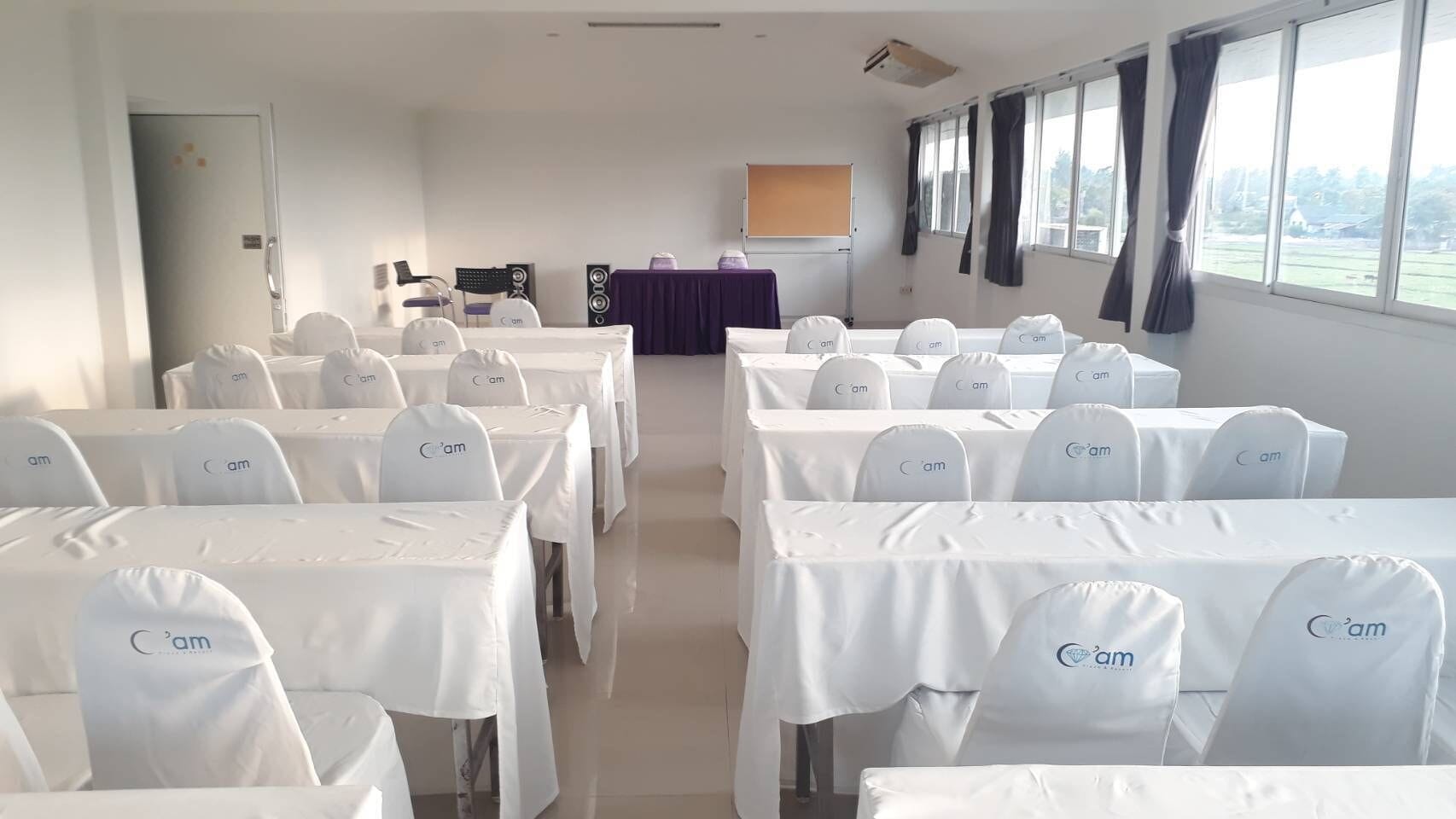 Un salón de conferencias con mesas y sillas dispuestas en filas, un atril y una pantalla de proyector.