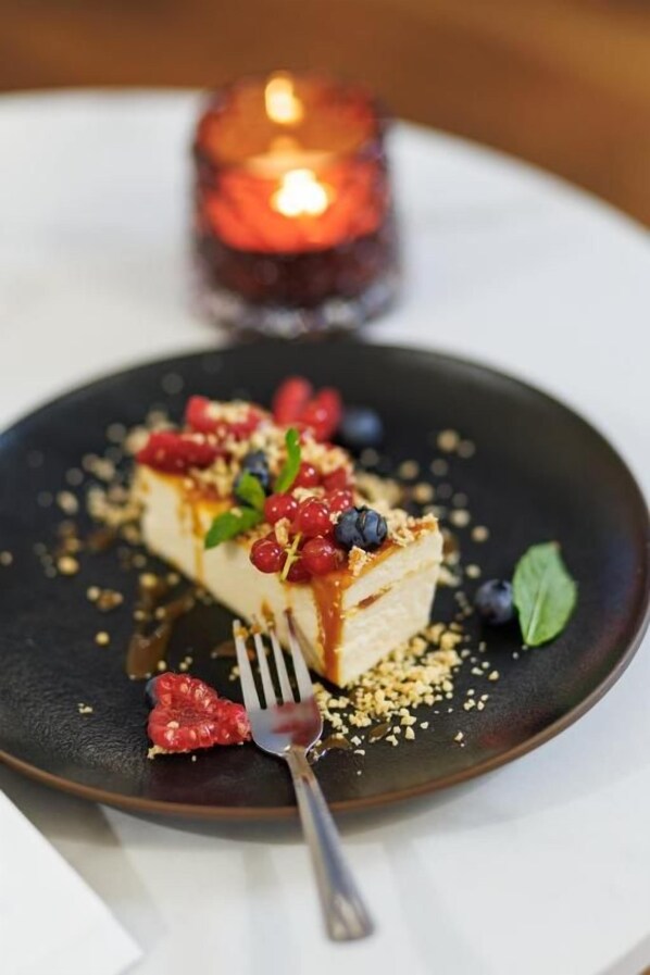 Postre en un plato con un tenedor, bayas y una vela al fondo.