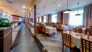 A spacious hotel dining area with multiple tables and chairs, a central walkway, and large windows with floral curtains. - Hotel 500 Stryków (Strykow)