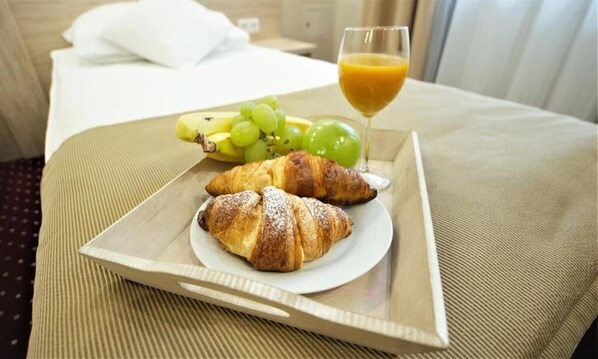 Bandeja con cruasanes, uvas, plátanos y un vaso de jugo de naranja sobre una cama.