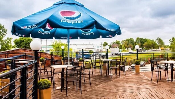 An outdoor patio area with tables and chairs, covered by a large blue Pepsi umbrella. - Hotel 500 Stryków (Strykow)