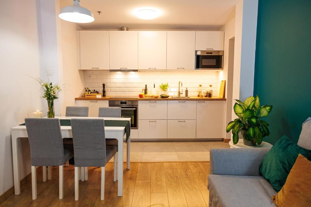 Una cocina moderna con gabinetes blancos, una mesa de comedor con sillas y una pequeña zona de estar con sofá y cojines.