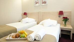 A hotel room with two beds, a tray of breakfast including croissants, fruit, and juice, and a vase with red flowers on the nightstand. - Hotel 500 Stryków (Strykow)