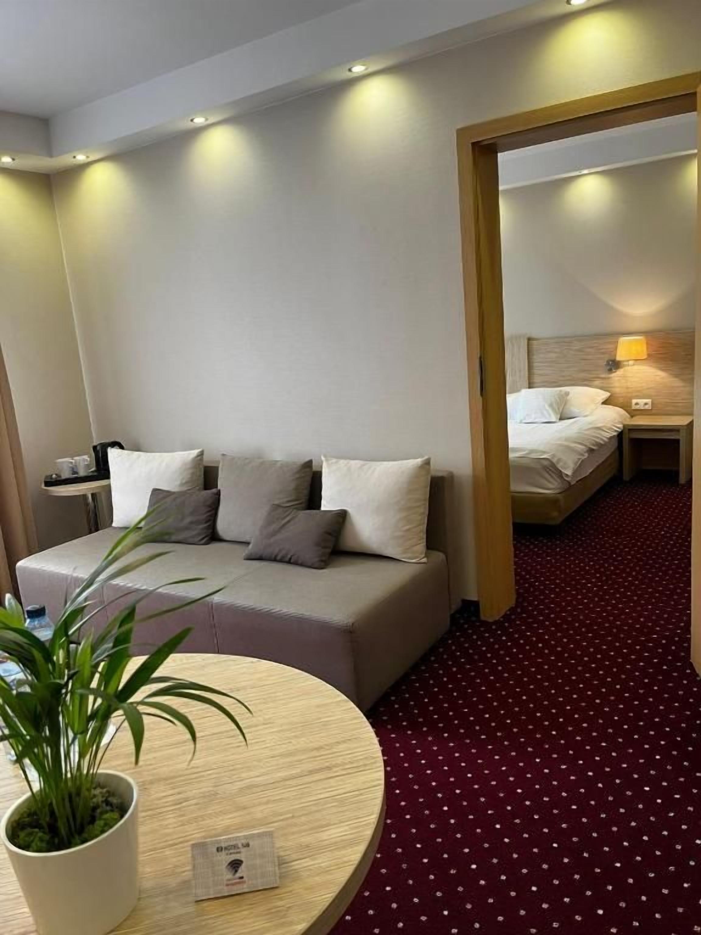 A hotel room with a sofa, a round table with a potted plant, and a bed with a nightstand.