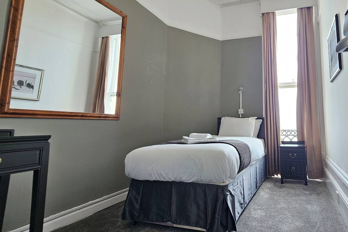 A bedroom with a bed, a dresser, a mirror, and a window with curtains.